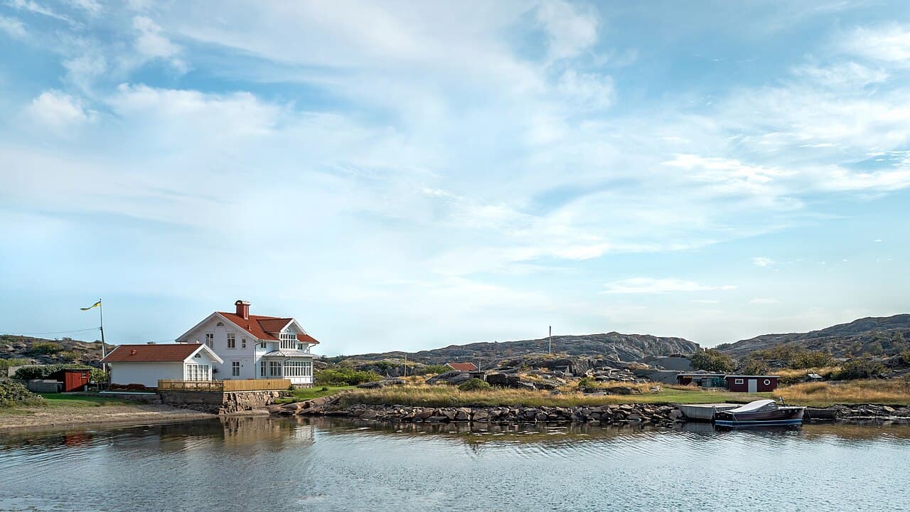 White wooden house with a small beach and an old motorboat of Pettersson type in Norra Grundsund, Lysekil…