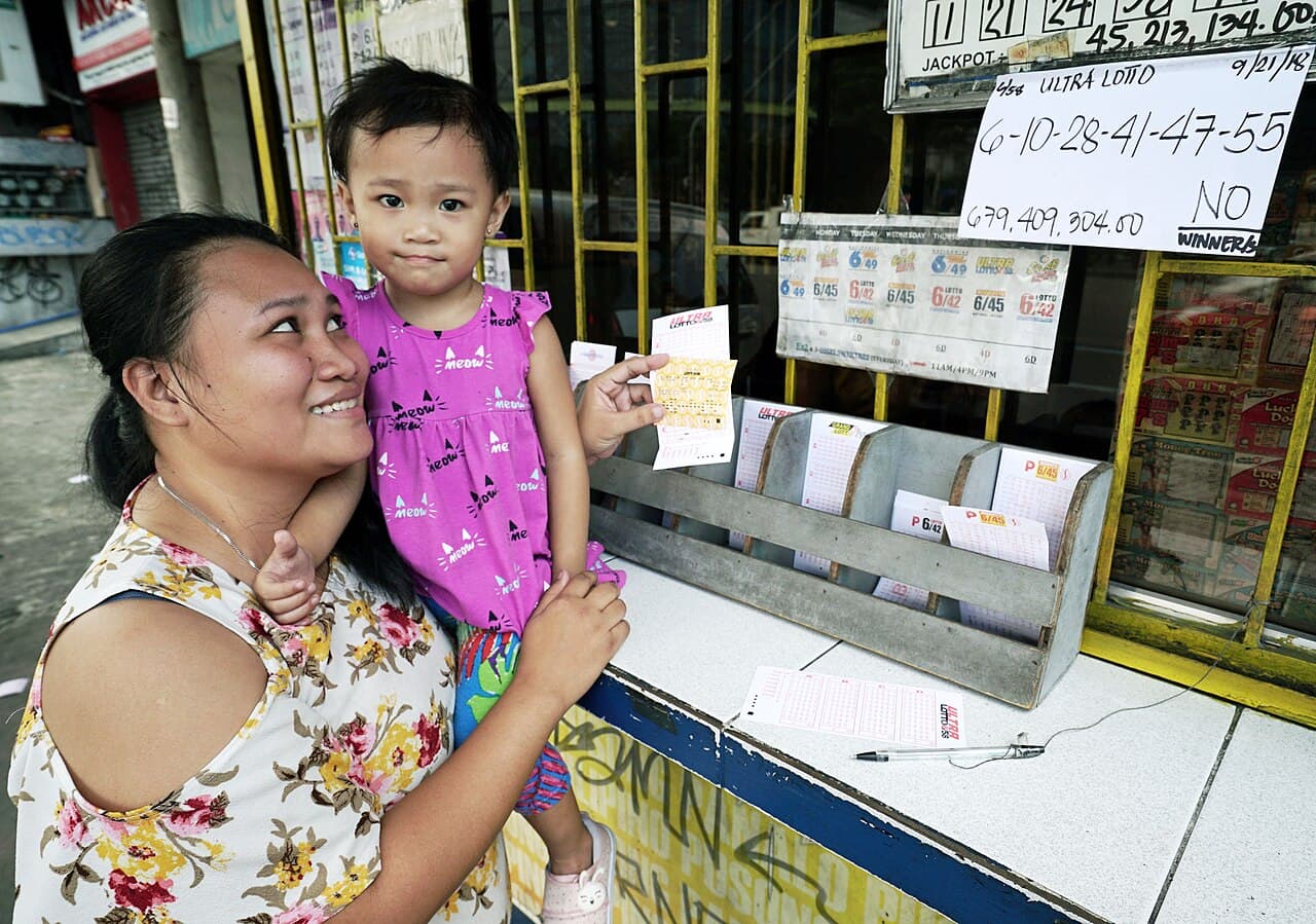 Jesamie Villacruses, 28, cuddles her daughter as she places her bet for the Ultra Lotto 6/58 draw with more than…